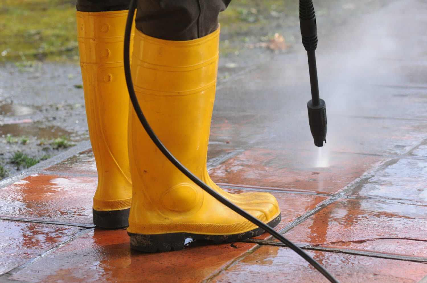 Hochdruckdüse und Gummistiefel auf einer nassen Steinfläche