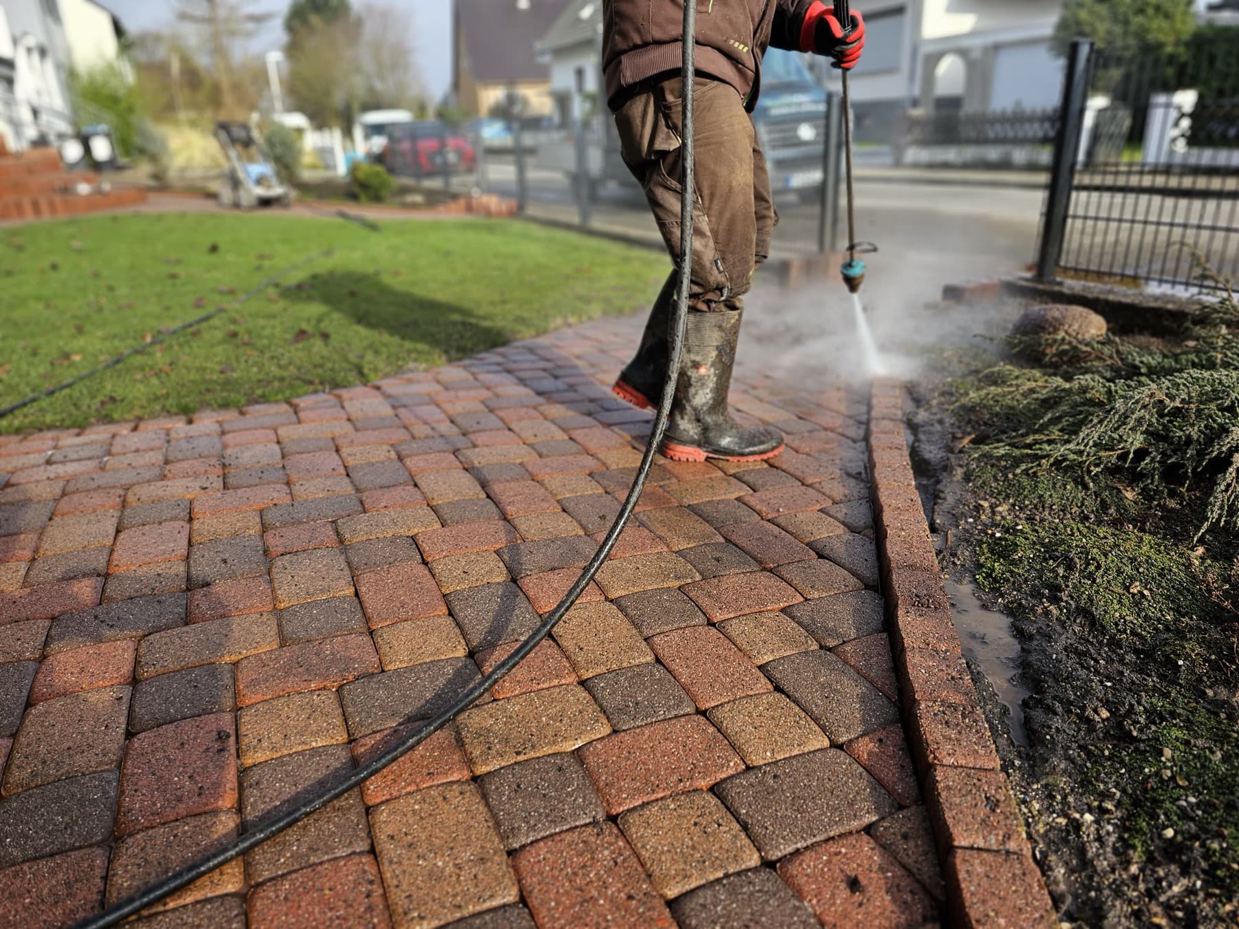 Reinigungskraft führt einen Hochdruckstrahler über einen Pflasterweg